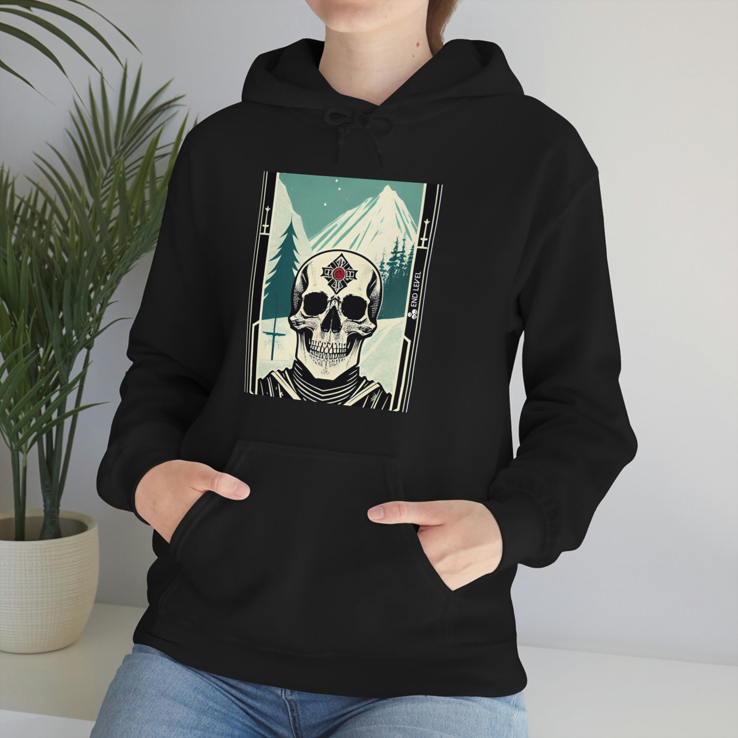 Woman with hands in black frostbite hoodie pouch beside plant.