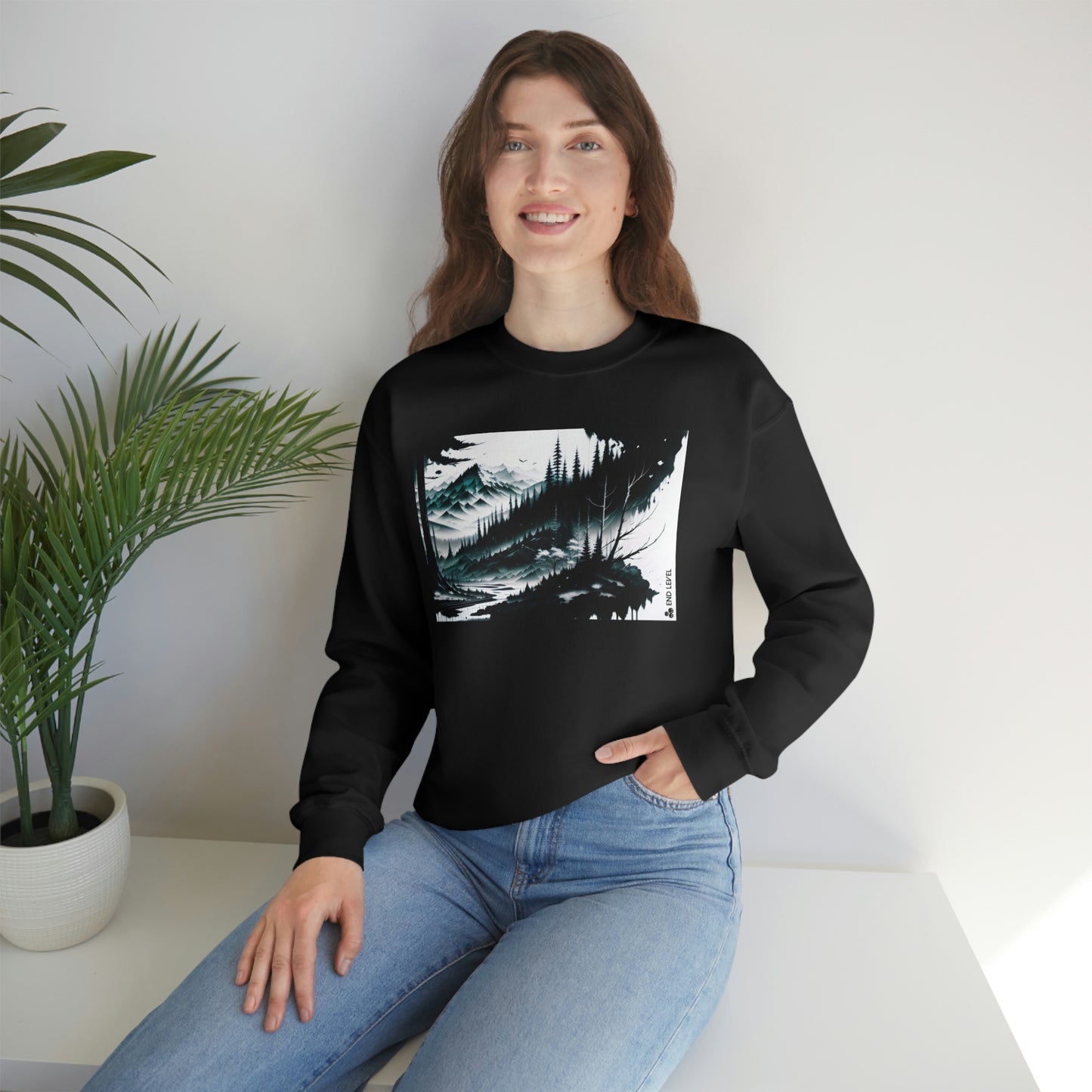 Woman with hand in jean pocket wearing black Grim Peak sweatshirt beside plant.