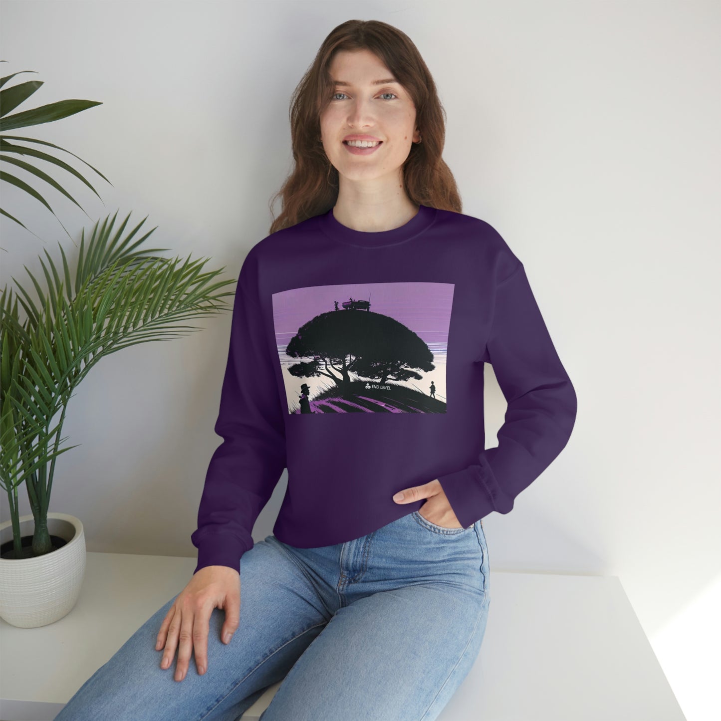 Woman with hand in jean pocket wearing purple Tough Parking sweatshirt beside plant.