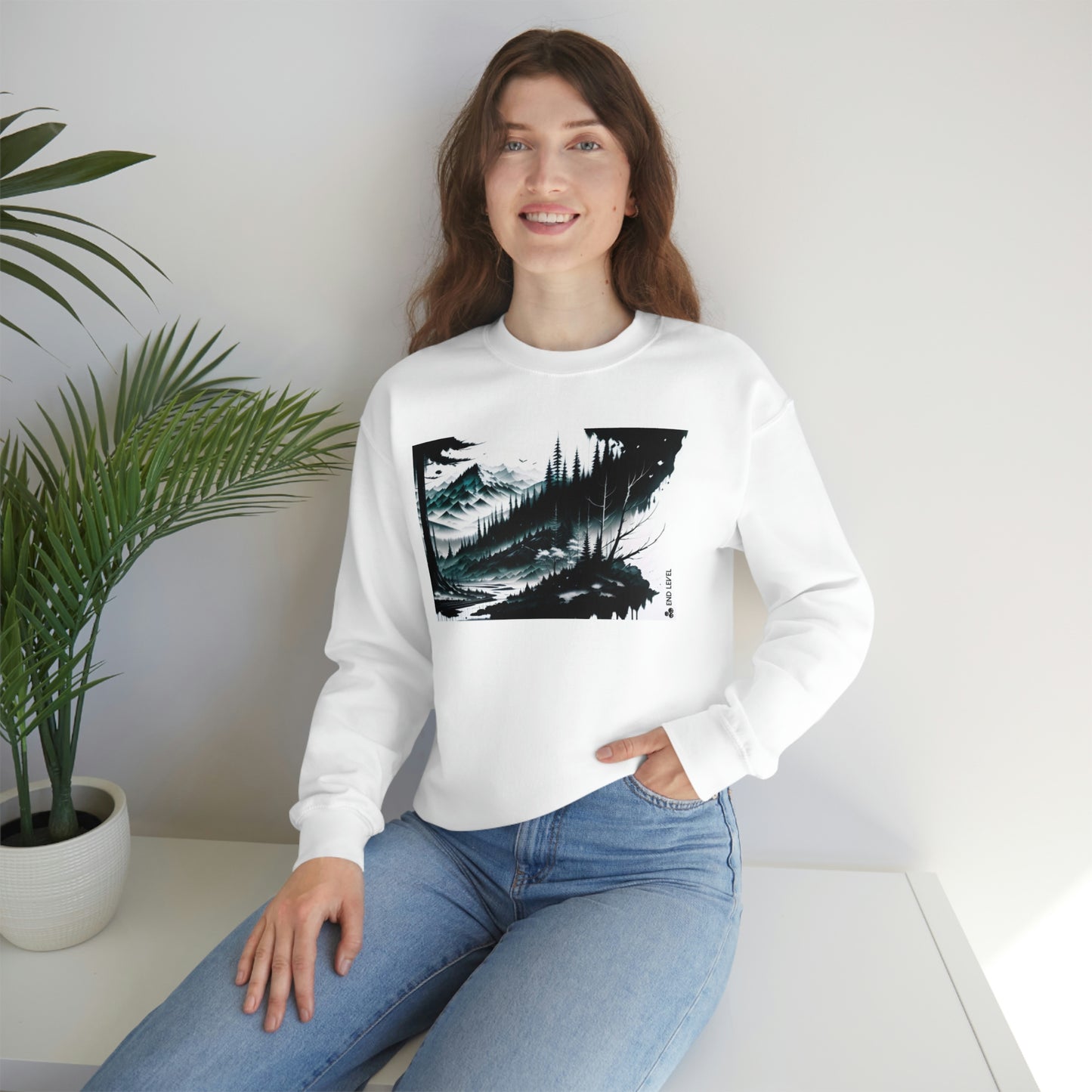 Woman with hand in jean pocket wearing white Grim Peak sweatshirt beside plant.