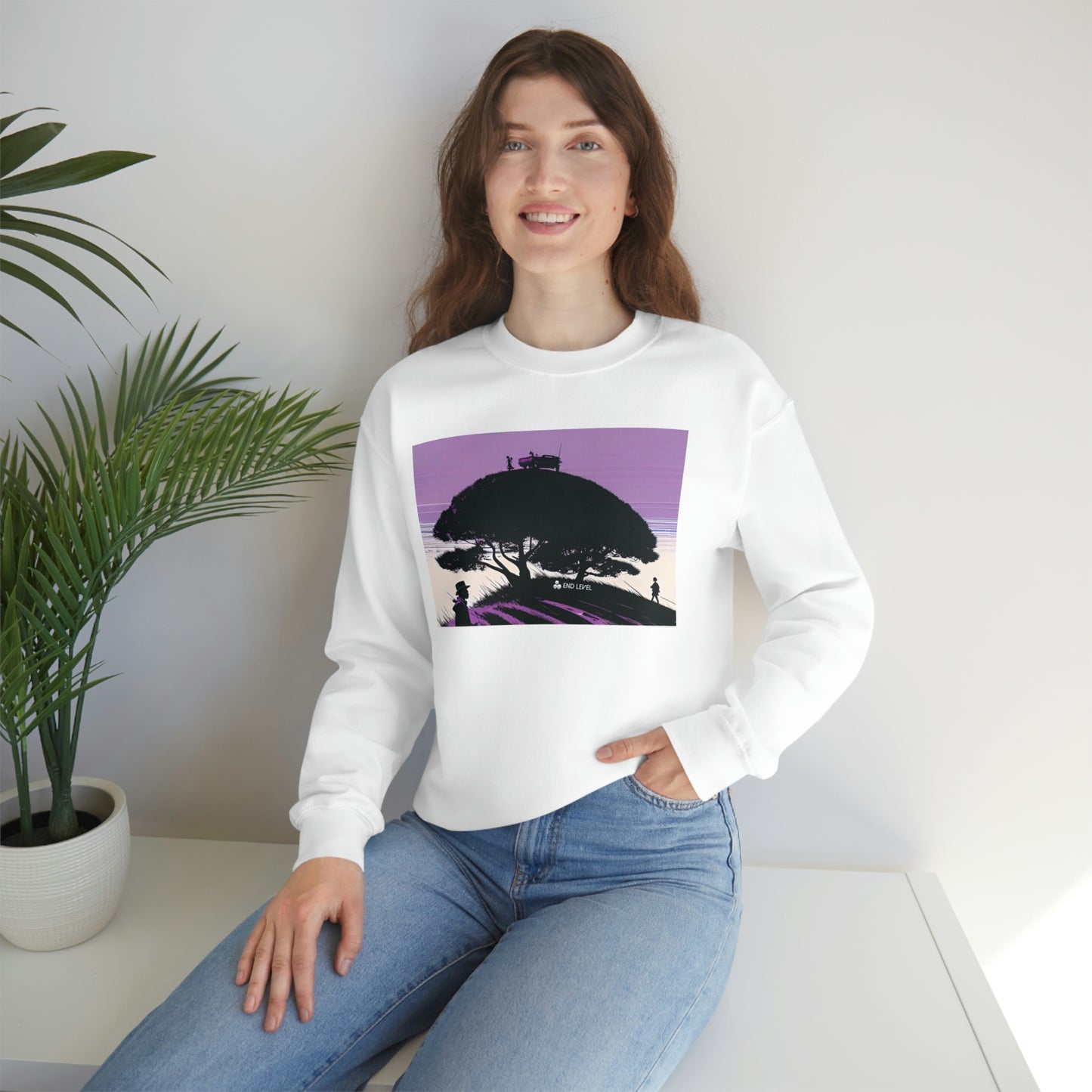 Woman with hand in jean pocket wearing white Tough Parking sweatshirt beside plant.